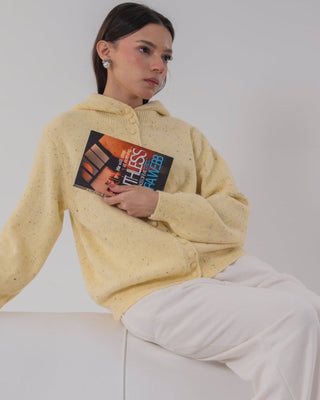 Person wearing a yellow hoodie with a graphic design, lying on a white couch.